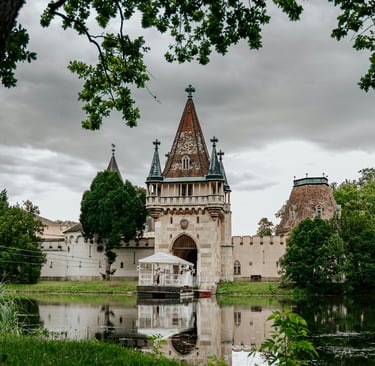 Laxenburg Castle Park featuring the historic Franzensburg castle reflected in a calm lake under a cloudy sky.