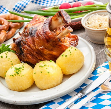 Roasted Bavarian pork knuckle served with potato dumplings, pretzels, and a glass of German beer.
