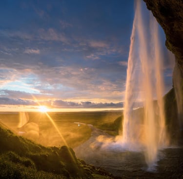 Seljalandsfoss waterfall in Iceland illuminated by a golden sunset with a dramatic sky.