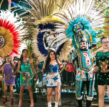 Dancers in colorful traditional costumes and feather headdresses at a vibrant street festival parade.