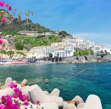 Panoramic view of Amalfi coast with pink bougainvillea flowers, white buildings, and blue sea.