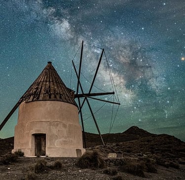 Rustic stone windmill under a vibrant Milky Way galaxy night sky in the Spanish countryside.