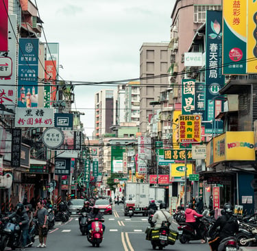 Busy city street in Taiwan with colorful business signs, parked scooters, and commuters on motorcycles.