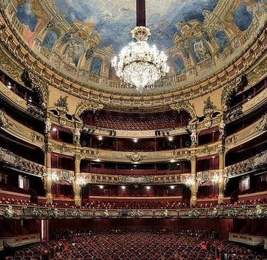 Ornate interior of a historic opera house featuring gold balconies, a painted ceiling, and a crystal chandelier.