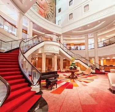 Grand luxury hotel lobby featuring a sweeping red carpet staircase and elegant piano lounge.
