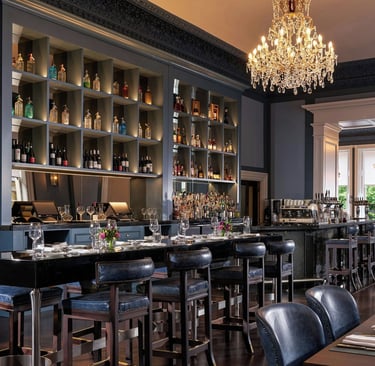 Elegant luxury bar and restaurant interior featuring leather stools, crystal chandeliers, and a backlit liquor shelf.