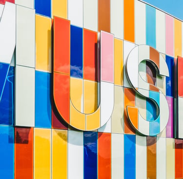 Modern museum building with a vibrant multi-colored glass facade and large 3D museum signage.