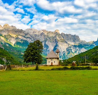 Small stone church in a green meadow with the Accursed Mountains in Theth, Albania.