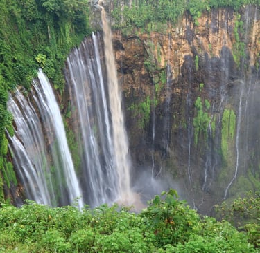 Panoramic view of Tumpak Sewu Waterfall in Indonesia surrounded by lush green tropical jungle.