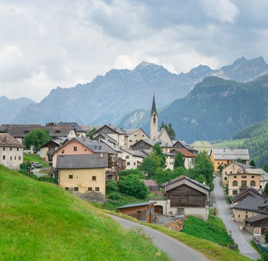 Panoramic view of a traditional Swiss mountain village in the Alps with a church tower and green hills.