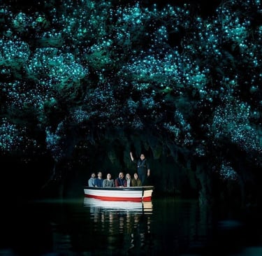 Tourists on a boat ride underneath bioluminescent glowworms in a dark New Zealand cave.