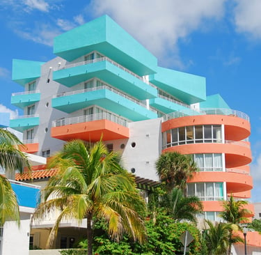 Colorful Art Deco hotel architecture in Miami Beach with teal and salmon balconies and palm trees.