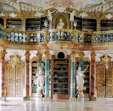 Ornate Baroque library interior with marble columns, gold accents, white statues, and historic books.
