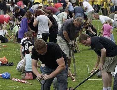 A large group of people participate in a worm charming competition on a grassy field.