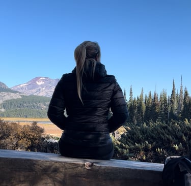 Anneke, zittend op een bankje, uitkijkend over bomen en een berg - het gevoel van vertragen