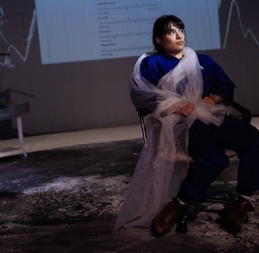 An Iranian woman in blue overalls sits, twisted in long white fabric