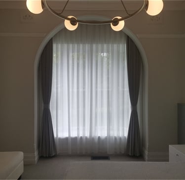 Elegant bedroom featuring a large arched window with white sheer curtains and blackout drapery.
