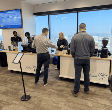 Customers ordering drinks at a Friday Coffee mobile espresso bar in a high-rise office with city views.