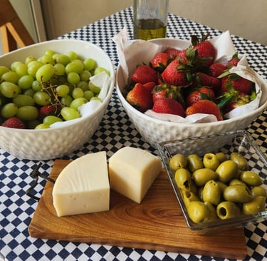 Fresh appetizers with green grapes, strawberries, olives, and cheese on a blue checkered tablecloth.
