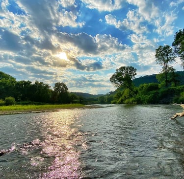 the root river with bluffs and treeline on the horizon, sun peaks through puffy clouds in a blue sky
