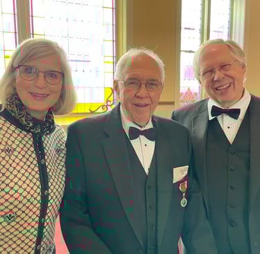 a smiling woman in a norwegian sweater stands next to two smiling men in tuxedos