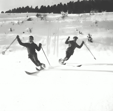 a blakc and white image of two men skiing toward the camera