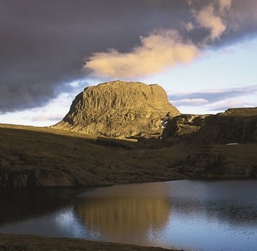 a lake in the foreground with a rock formation on the horizon