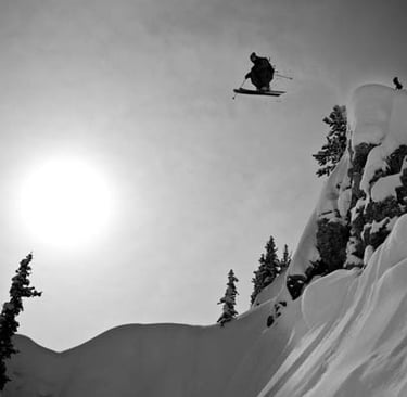 a black and white photo of a snowy slope and a man on skis in the air