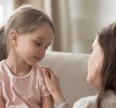 a woman in a pink shirt is resting her hand on a little girl's shoulder