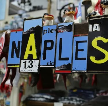 Insegna decorativa con la scritta “Naples” in un negozio di souvenir, usata come immagine hero per l