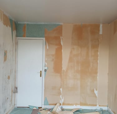 Une pièce en cours de rénovation montrant des murs avec du papier peint arraché, des débris sur le s