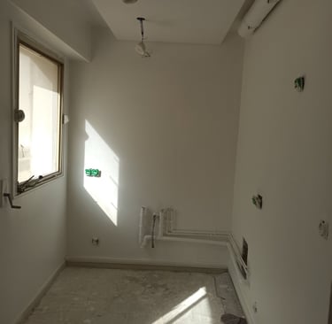 Pièce vide en rénovation avec murs blancs, tuyaux de plomberie apparents et câblage électrique