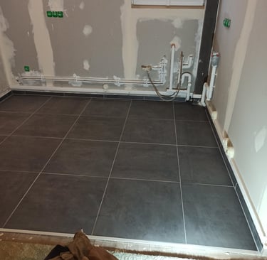 Installation de carrelage gris foncé dans une pièce en rénovation avec plomberie et prises électriqu