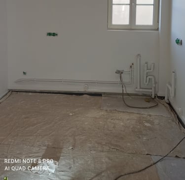 Une cuisine en cours de rénovation avec des tuyaux de plomberie apparents, des prises électriques et
