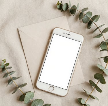 Flat lay of a blank smartphone mockup on a paper envelope with eucalyptus leaves on a beige fabric background.