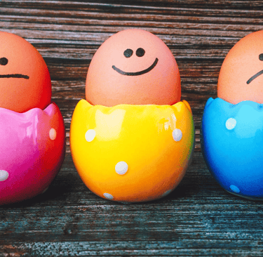 neutral, happy, sad face drawn on eggs in colourful egg cups