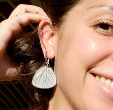 A butterfly earring in a woman's ear. She is smiling.