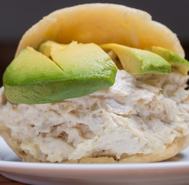 Reina Pepiada arepa stuffed with creamy chicken salad and fresh avocado slices on a white plate.
