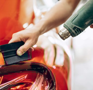 Stiklų tamsinimo paslaugų teikėjas naudoja šilumos pistoletą automobilio galiniam žibintui.