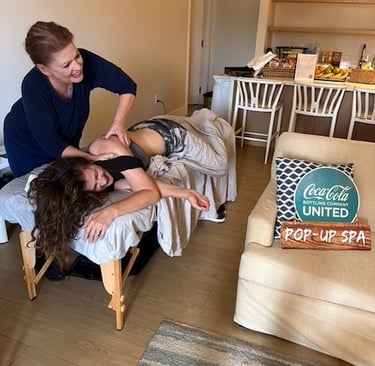 Professional massage therapist providing a shoulder treatment at a Coca-Cola United pop-up spa event.