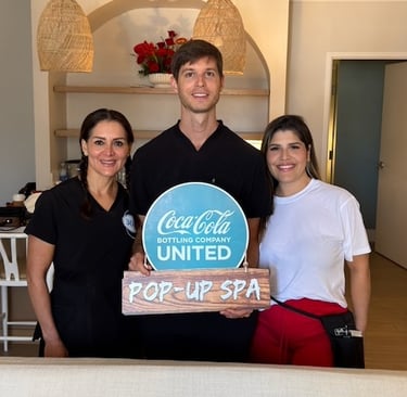 Three spa professionals posing with a Coca-Cola Bottling Company United pop-up spa sign.