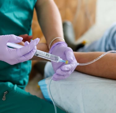 Nurse in green scrubs and purple gloves administering IV therapy blend through a patient's IV line.