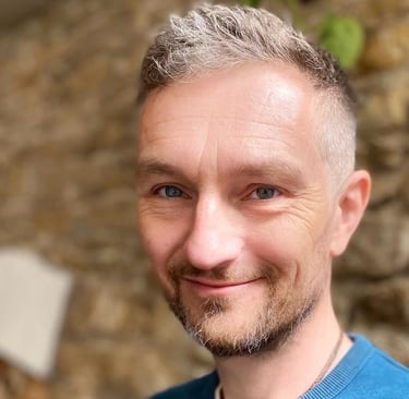 A picture of Chris, who sports short hair and neat stubble. Chris smiles directly into the camera.