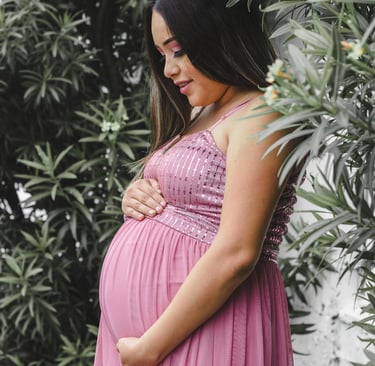 a pregnant woman wearing a pink dress in front of some tropical plants