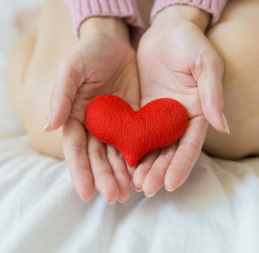 a felt heart being held in a person's hands while they are kneeling on a bed