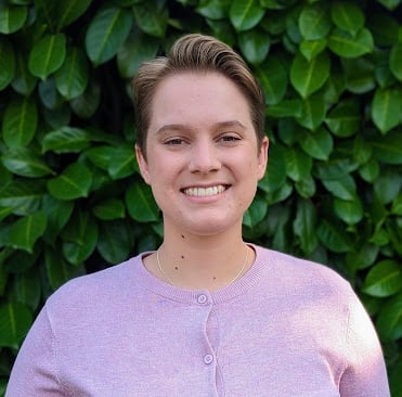 a headshot of a woman with a short haircut in front of a bush