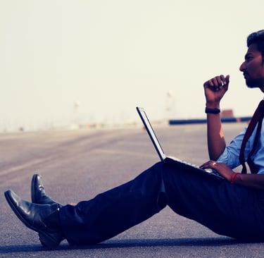 homem-de-gravata-sentado-na-estrada-pensativo-com-computador-no-colo