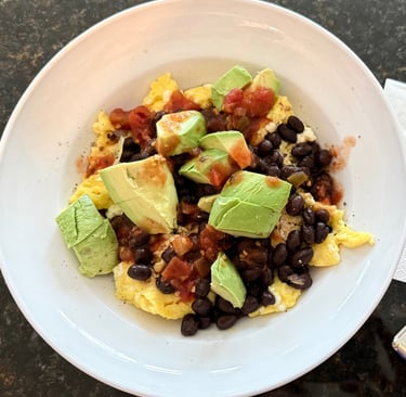 Scrambled eggs with black beans, avocado, and salsa in a white bowl.