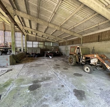 the inside of a large barn with rusting old tractors and farm machinery