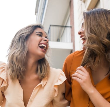 Dos hermanas adultas riendo y abrazadas, felices con su canción personalizada de Musycol.